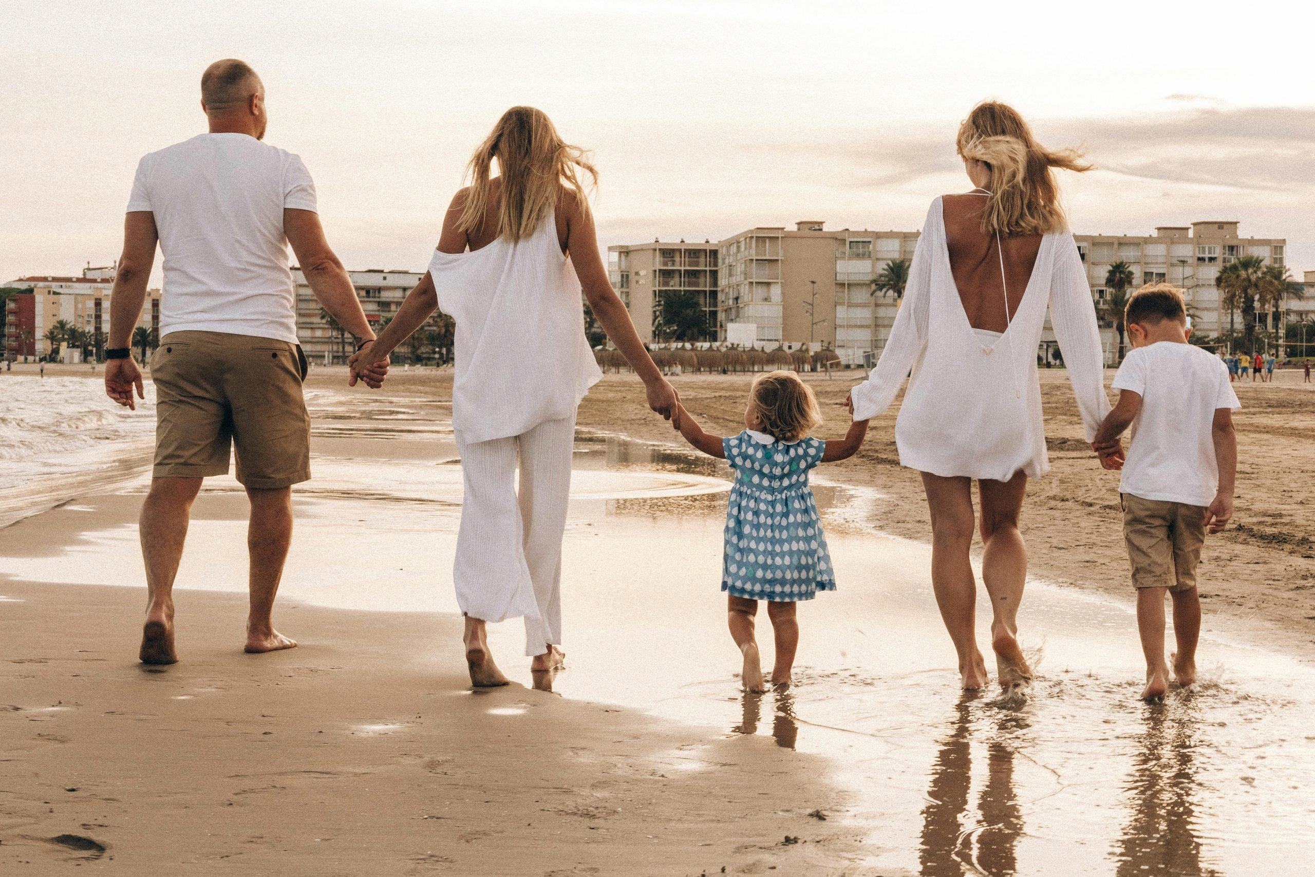 A family of five people walk along the beaches edge.